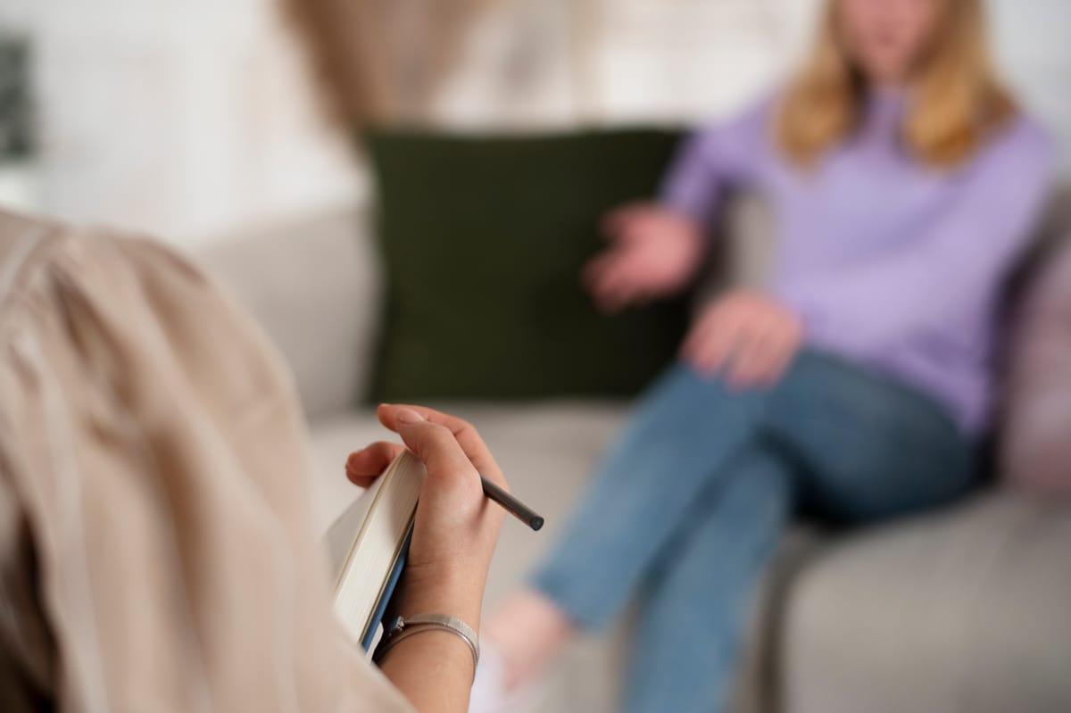 Therapist taking notes while listening to a client during a traditional talk therapy session.