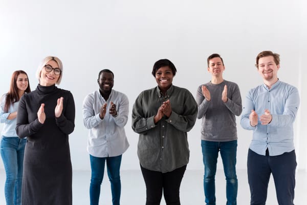Smiling diverse group clapping in support, symbolizing approval-seeking and social validation dynamics.